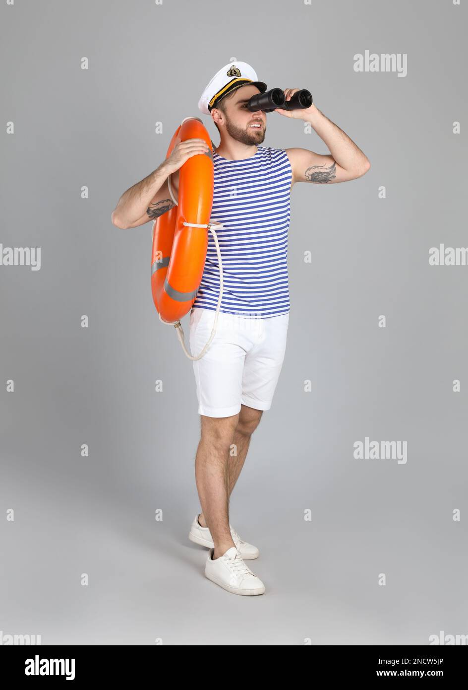 Sailor with binoculars and ring buoy on light grey background Stock Photo