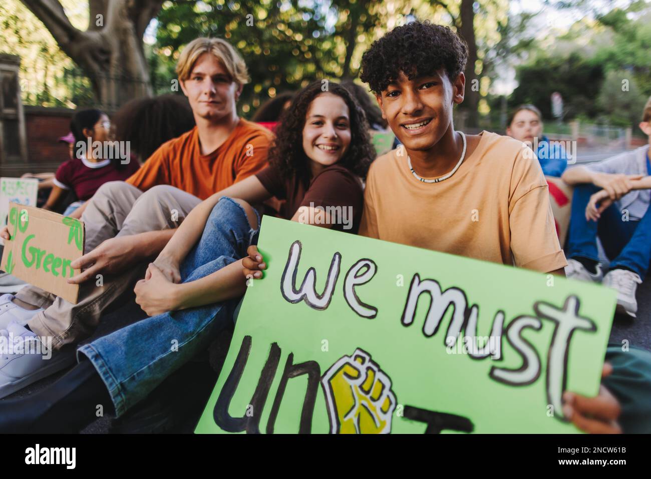 Group of multicultural teenage activists holding posters while sitting at a climate change protest. Happy young people calling for unity during a glob Stock Photo