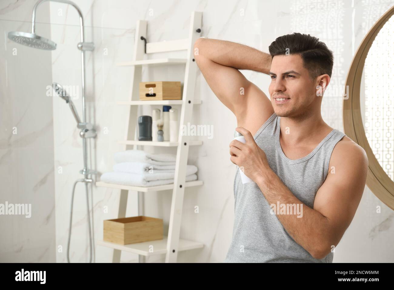 Handsome Man Applying Deodorant To Armpit In Bathroom Space For Text handsome-man-applying-deodorant-to-armpit-in-bathroom-space-for-text