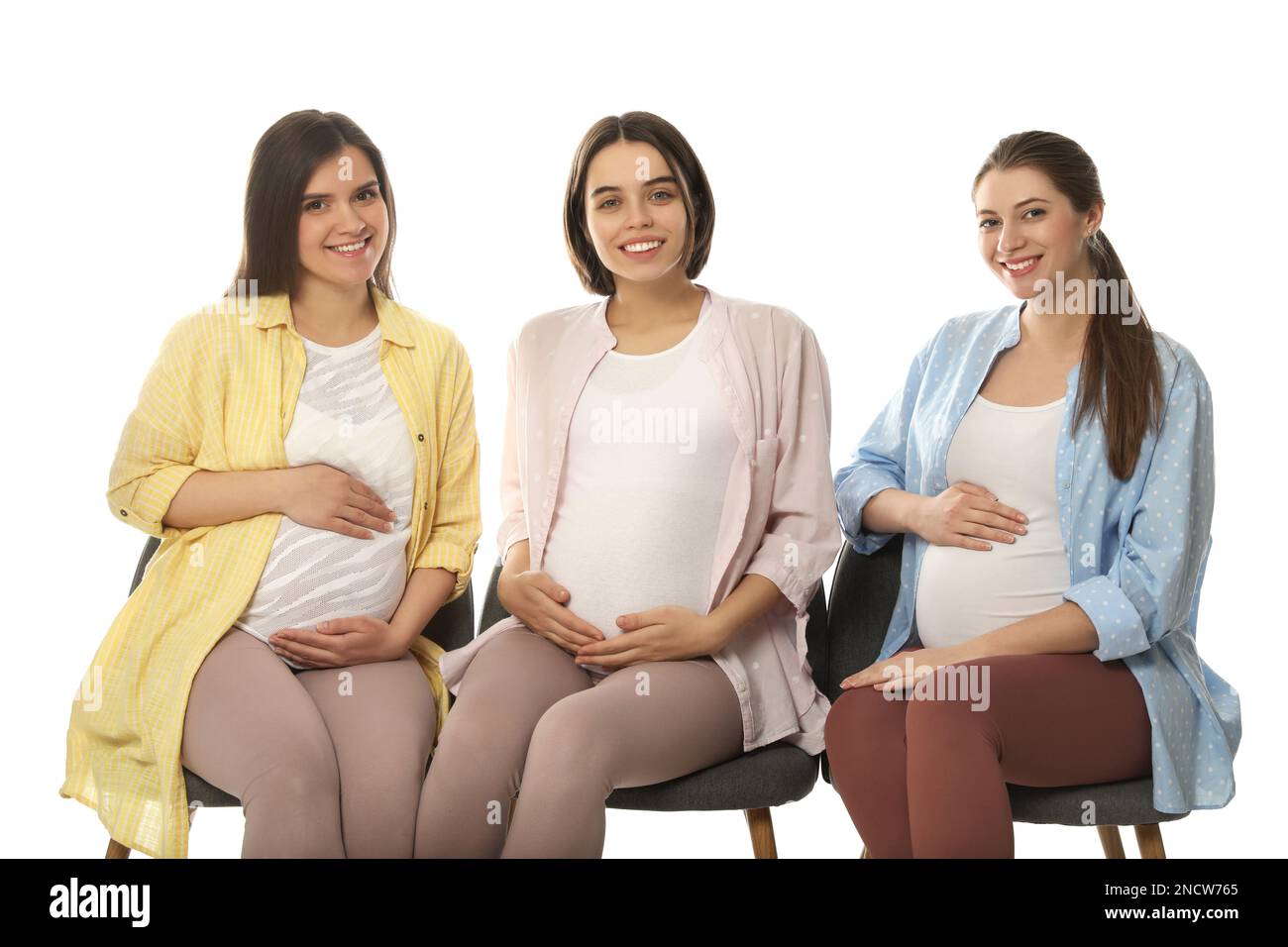 Happy pregnant women sitting on chairs against white background Stock