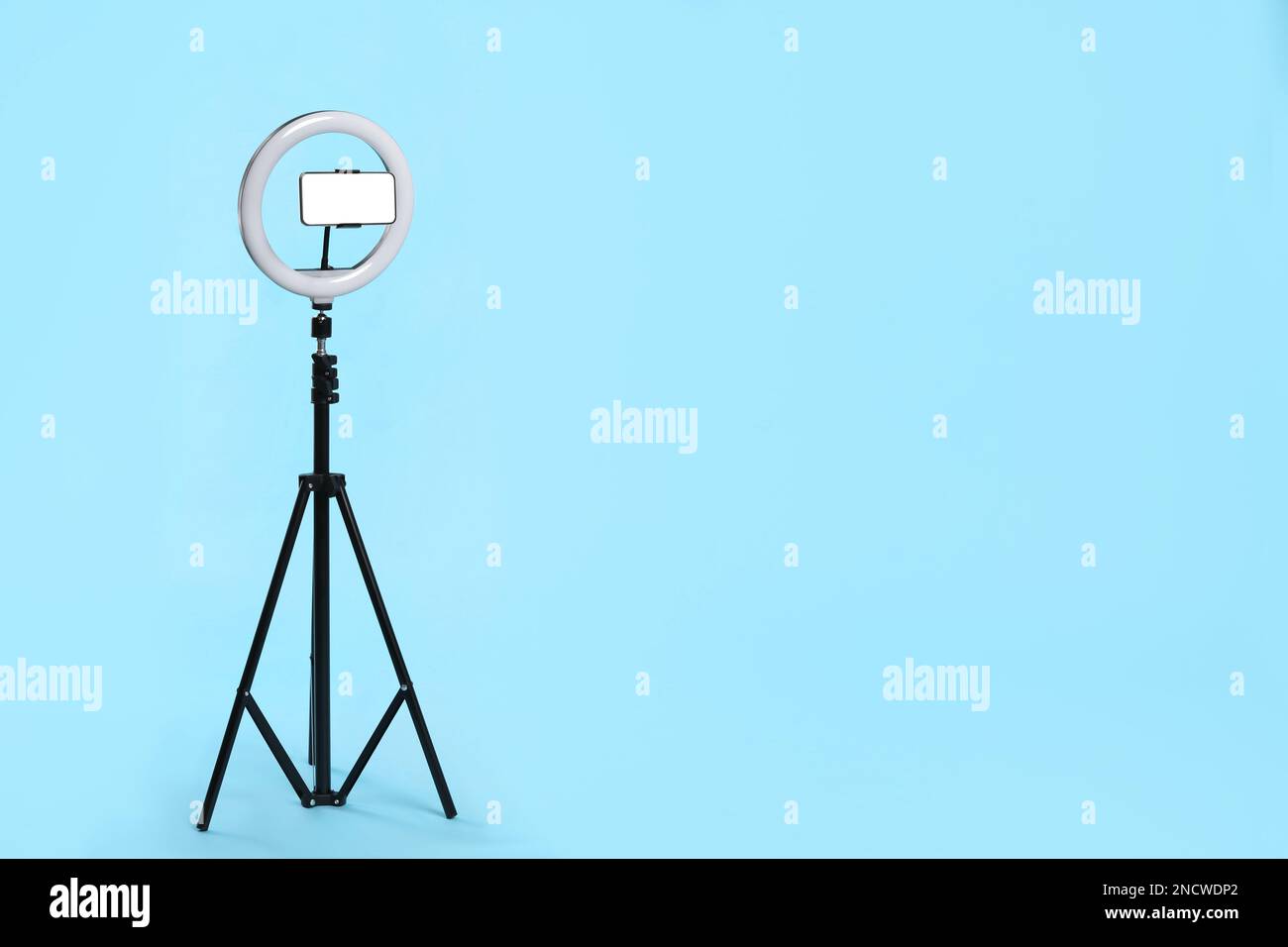 Modern tripod with ring light and smartphone on light blue background ...