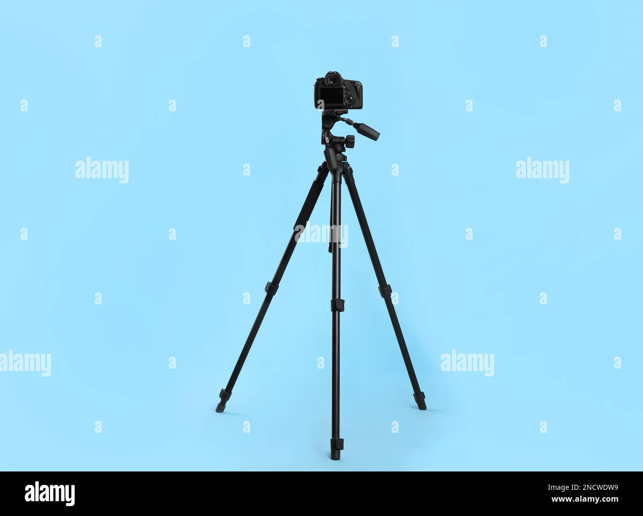 Modern tripod with professional camera on light blue background Stock ...
