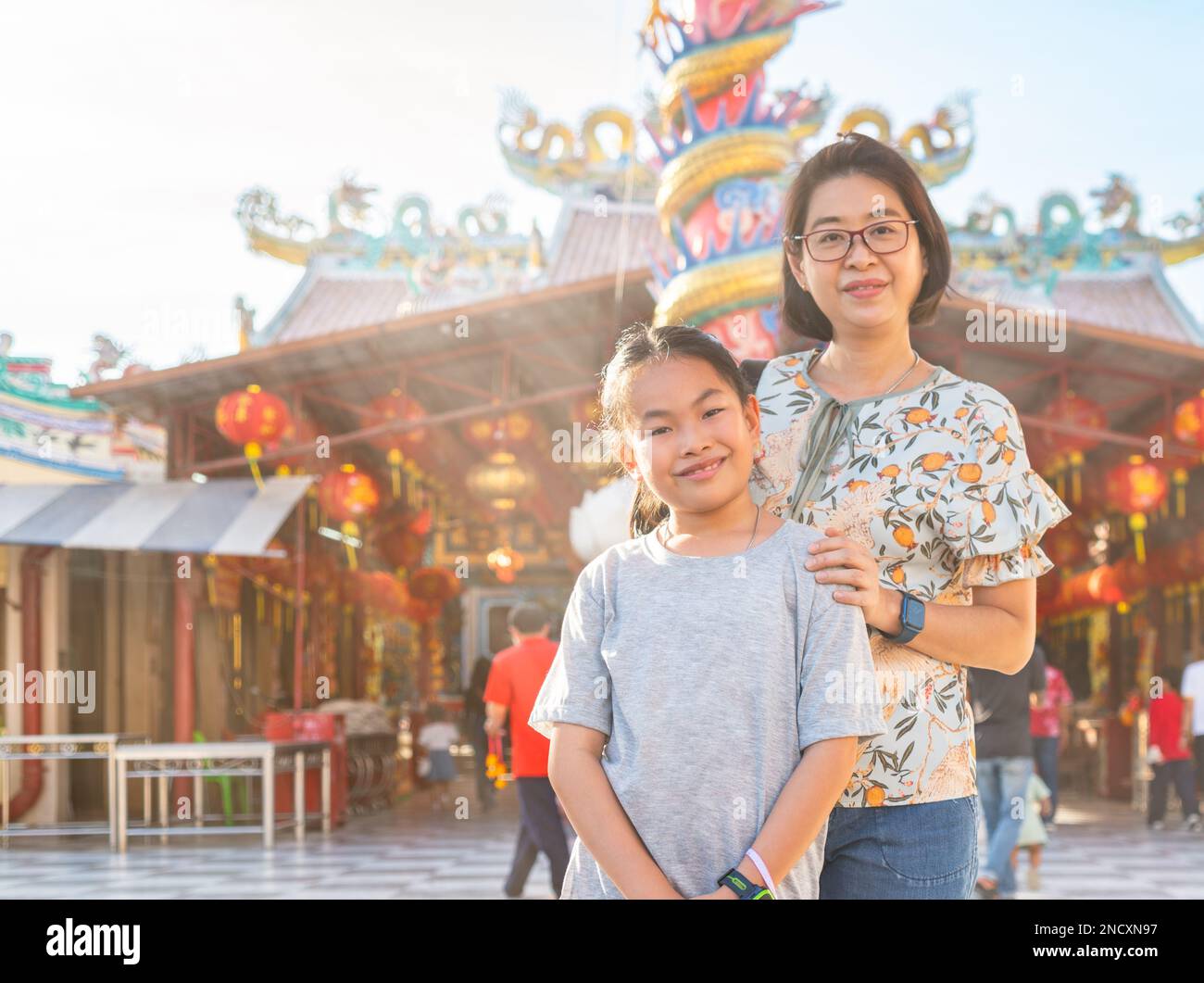 Asian child girl at 8 or 9 years old stands with a middle-aged mother in front of a blurred Chinese temple background, sunlight in the evening, lookin Stock Photo