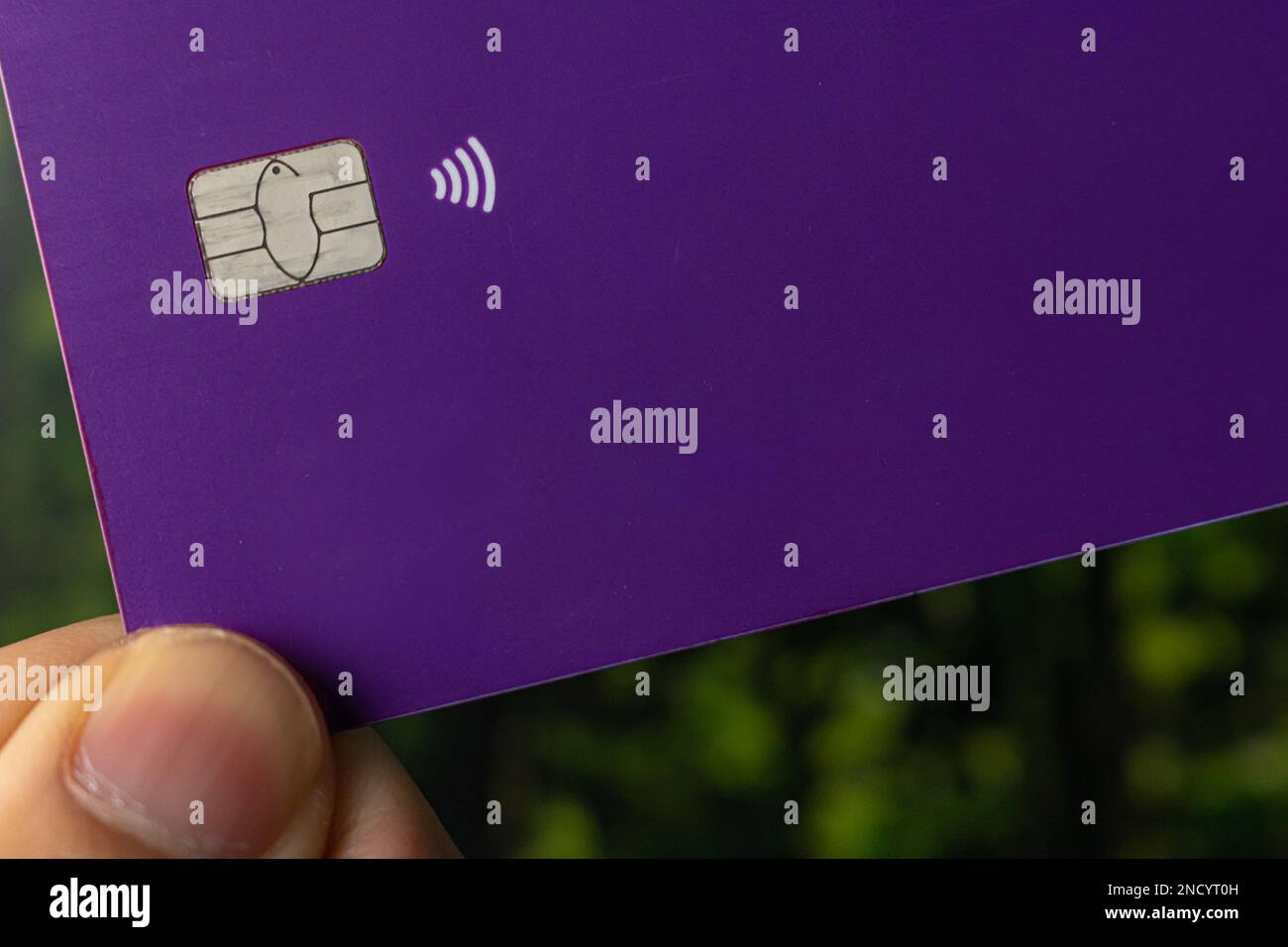 fingers holding a purple credit card with contactless technology and a chip Stock Photo