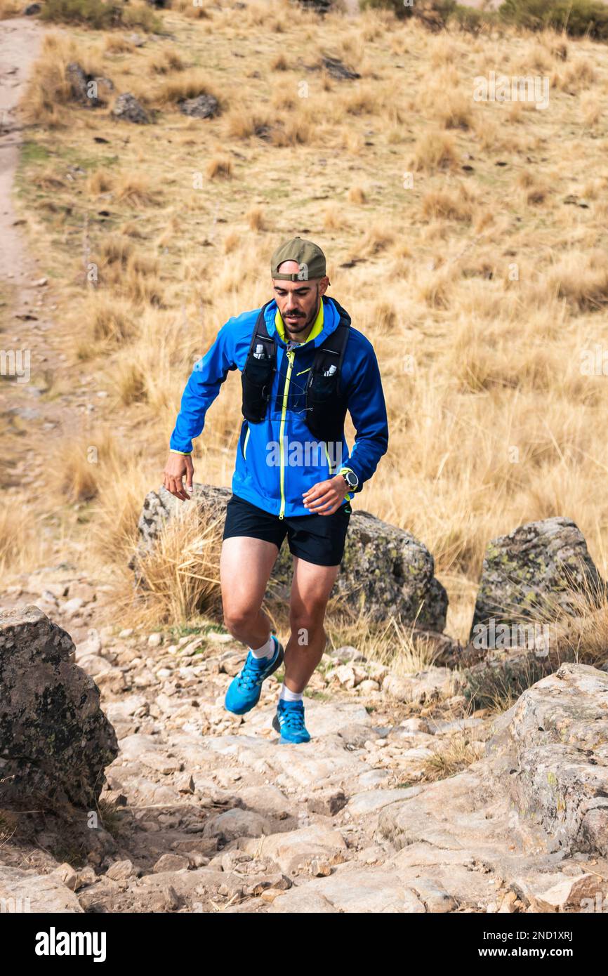 Young man practising trail running in the high mountains, while climbing to the top of the mountain. Stock Photo