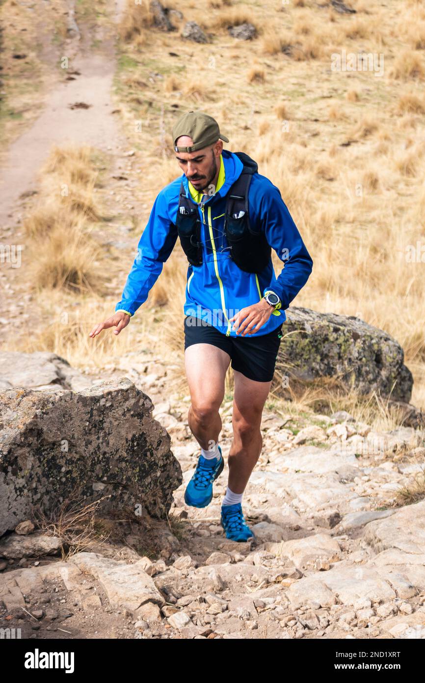 Young man practising trail running in the high mountains, while climbing to the top of the mountain. Stock Photo