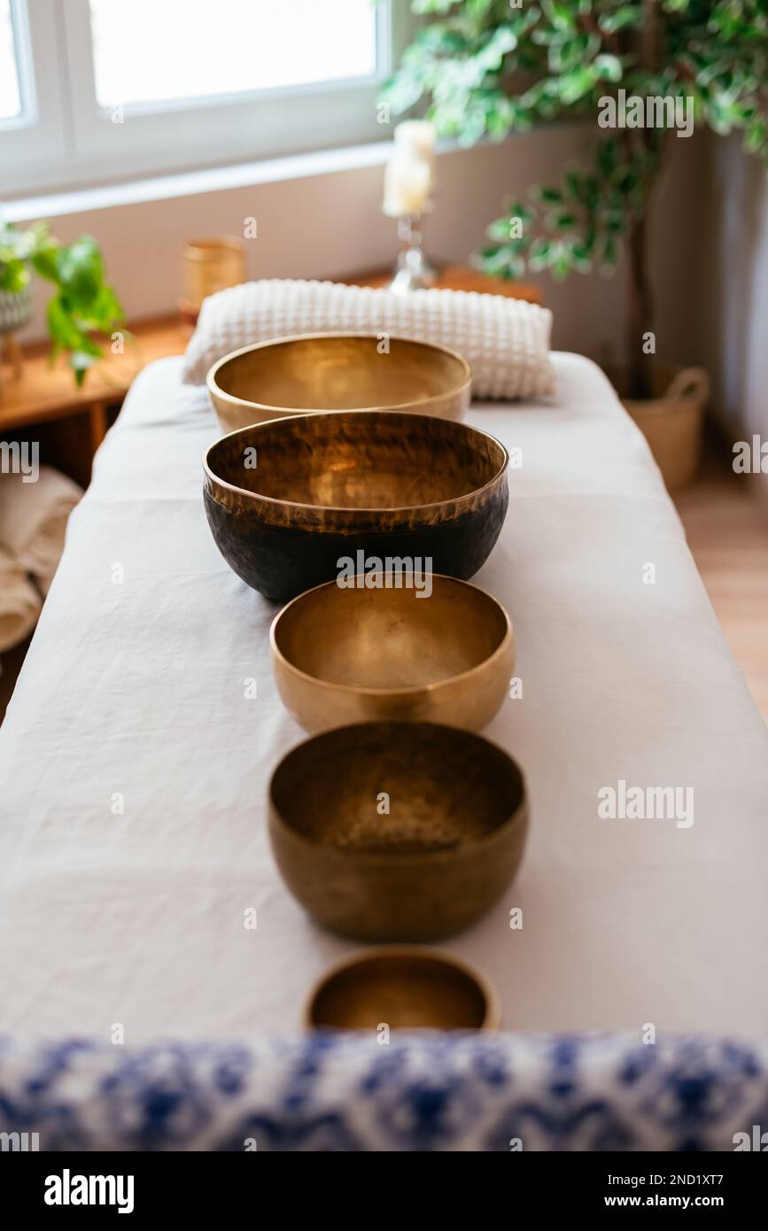 High angle of Tibetan singing bowls arranged in row on white massage bed at cozy spa salon Stock Photo