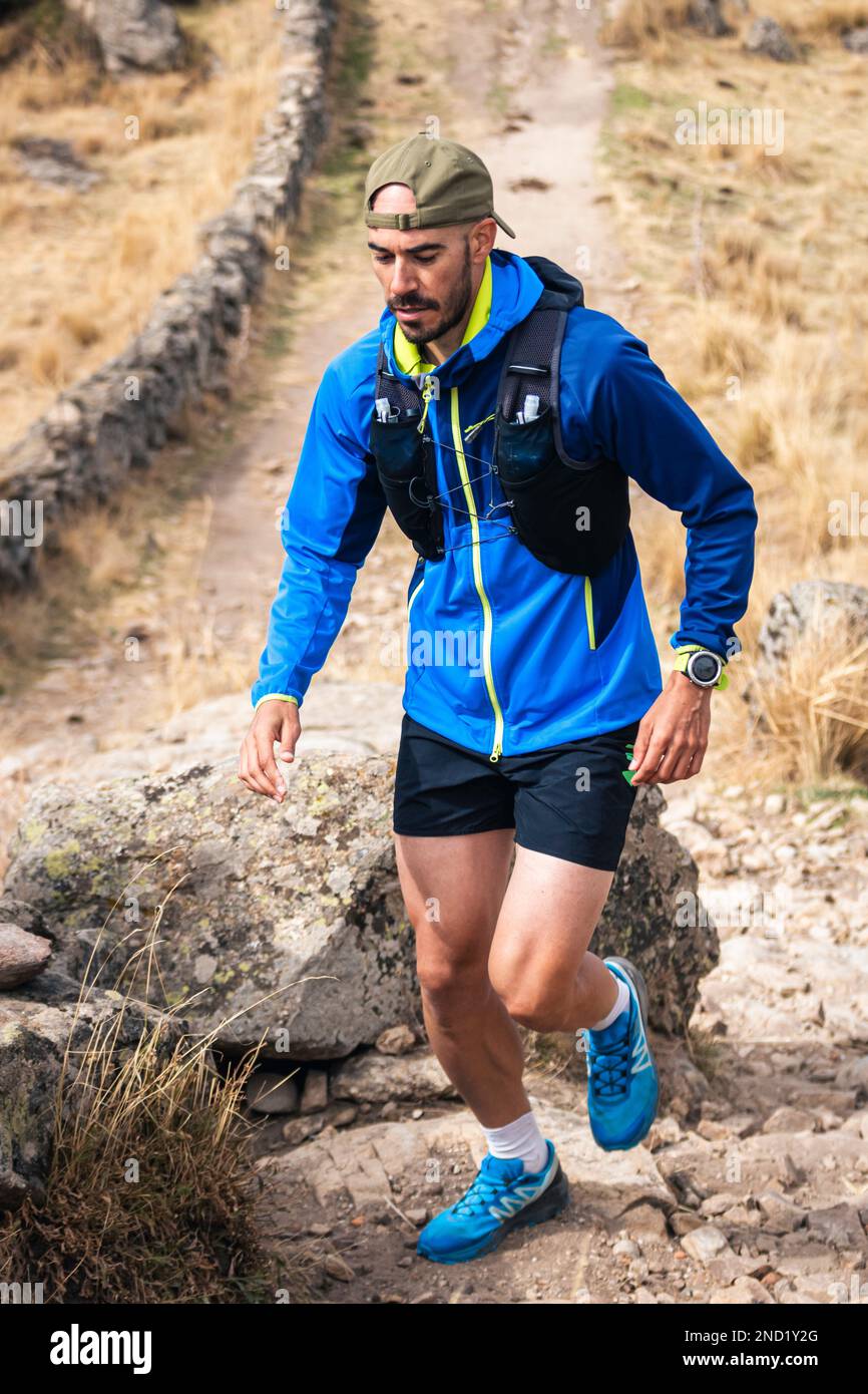 Young man practising trail running in the high mountains, while climbing to the top of the mountain. Stock Photo