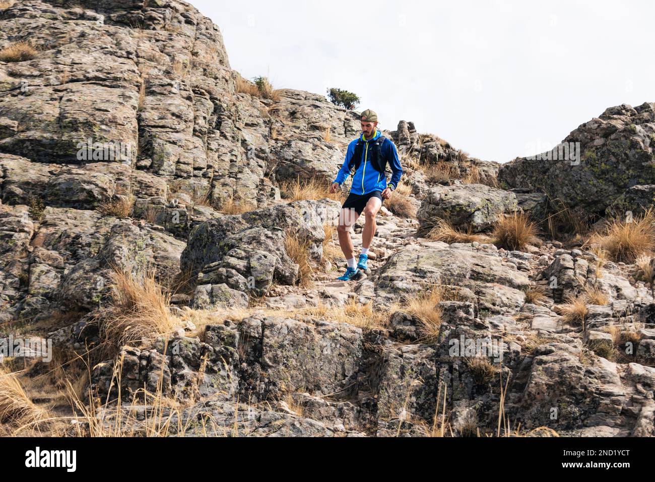 Young man practising trail running in the high mountains, while descending down the mountainside Stock Photo