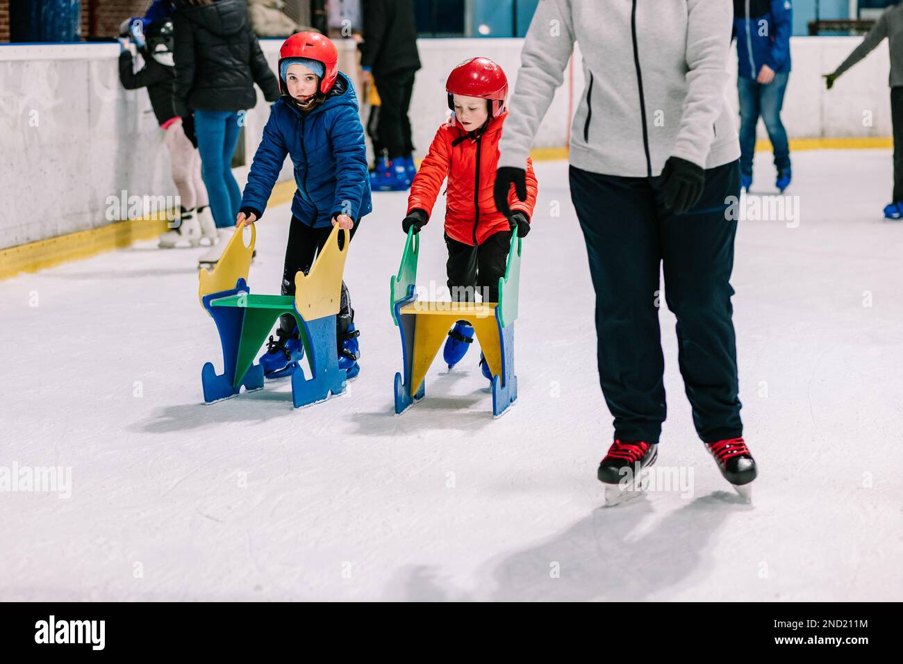 Cute children in outerwear and protective helmets pushing helpers while