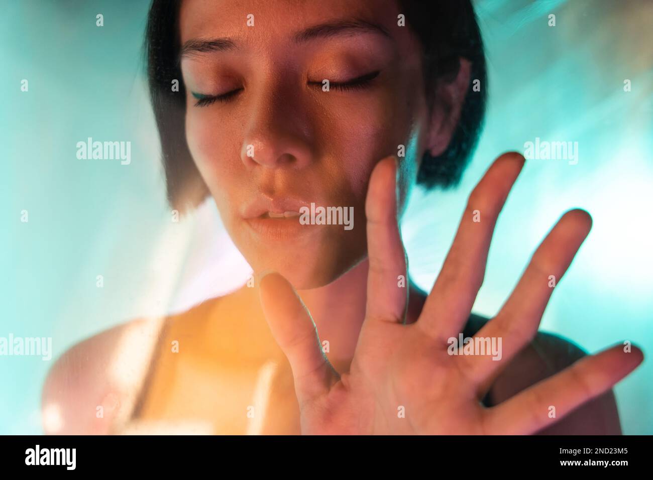 Through glass of confident young female with short hair and eyes closed while showing stop gesture Stock Photo