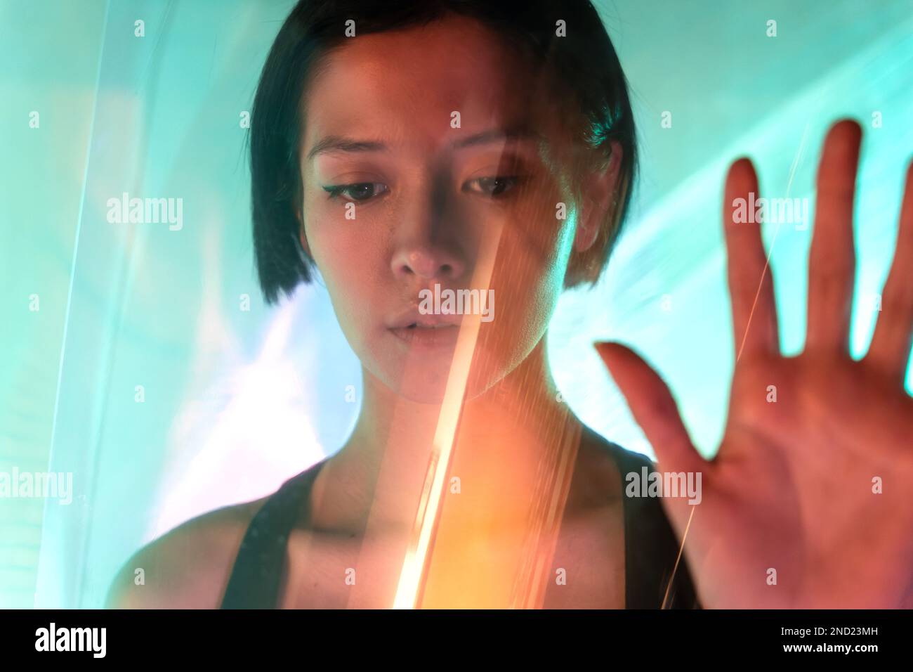 Through glass of confident young female with short hair and brown eyes looking down while showing stop gesture Stock Photo