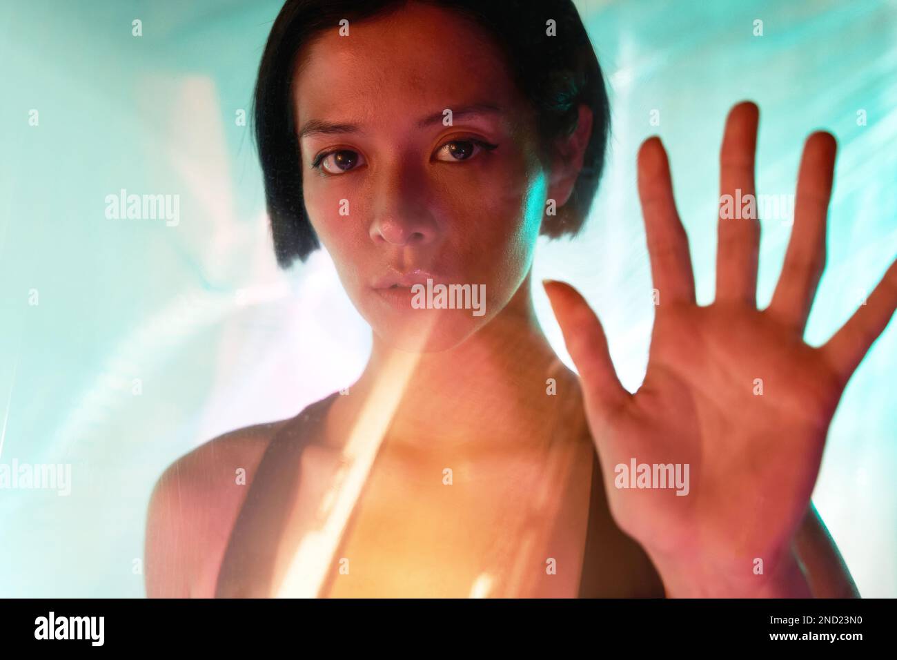 Through glass of confident young female with short hair and brown eyes looking at camera while showing stop gesture Stock Photo