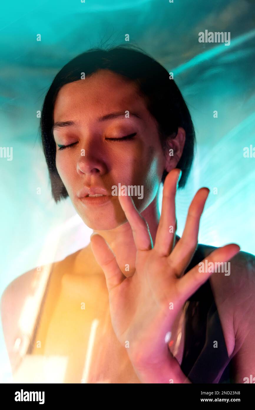 Through glass of confident young female with short hair and eyes closed while showing stop gesture Stock Photo