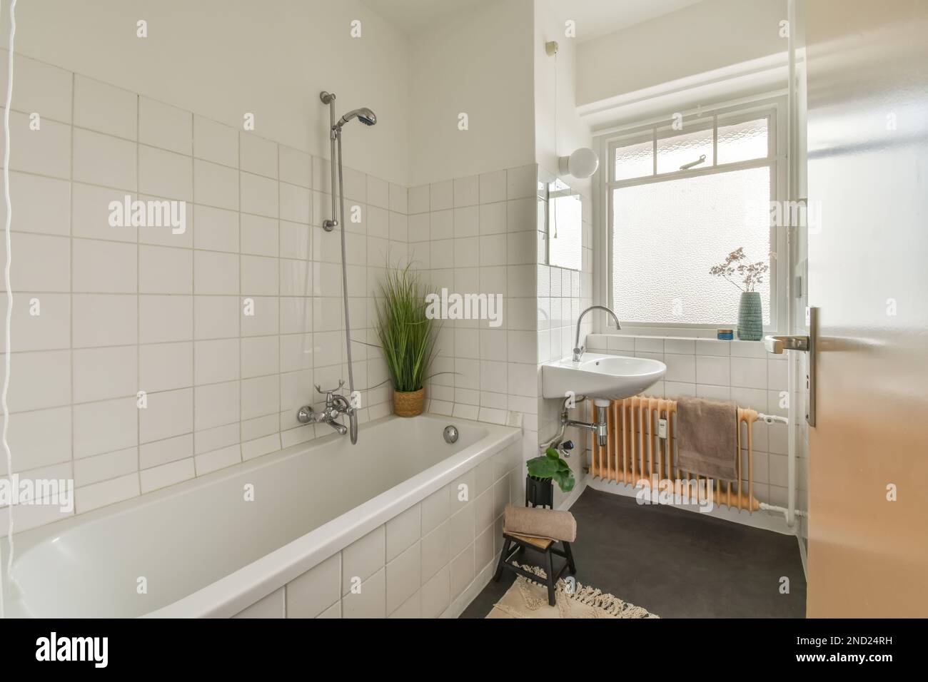 Bathtub with shower placed near sink under mirror against window and
