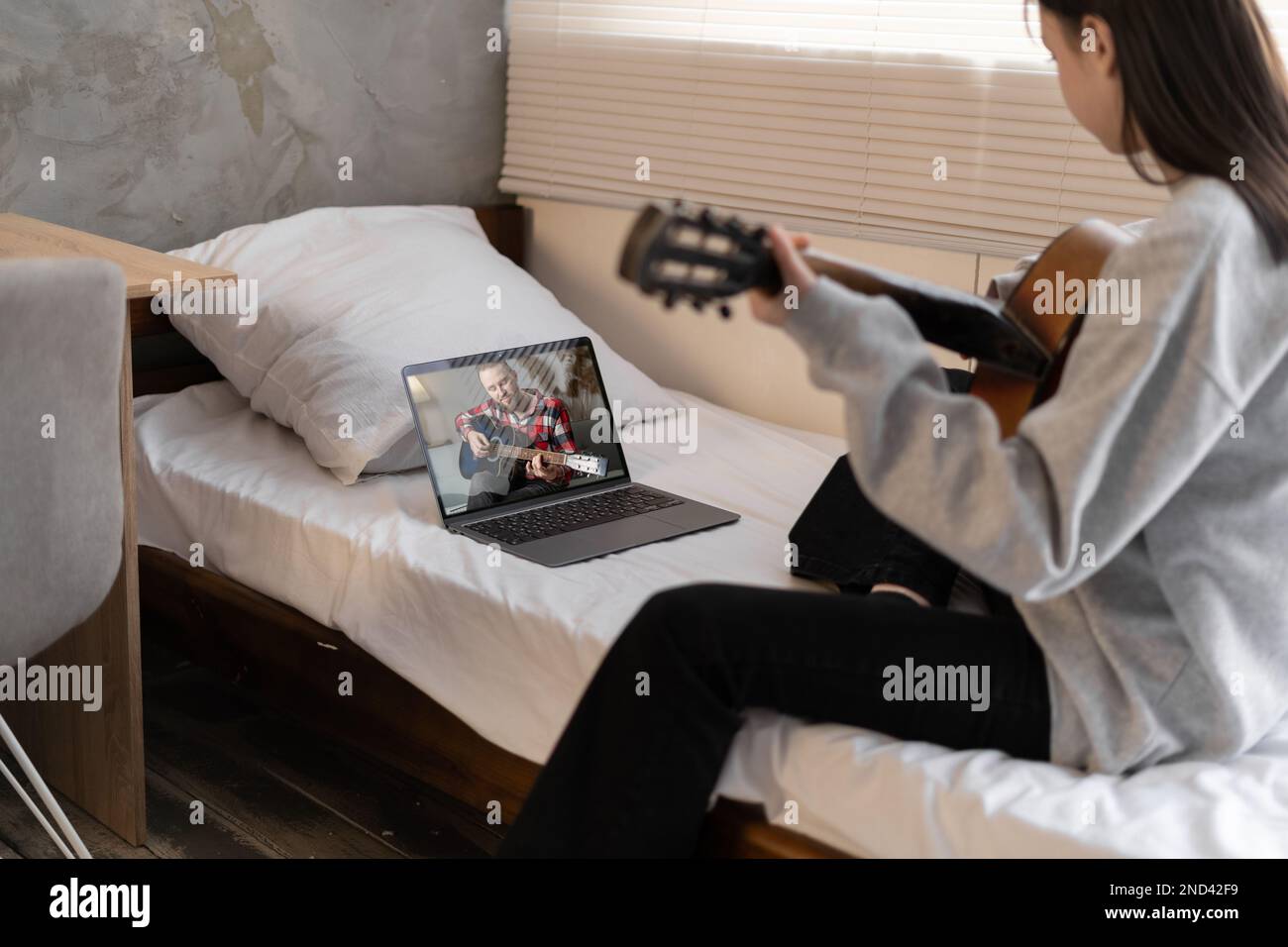 Young asian girl playing guitar sitting on bed watching video tutorial ...