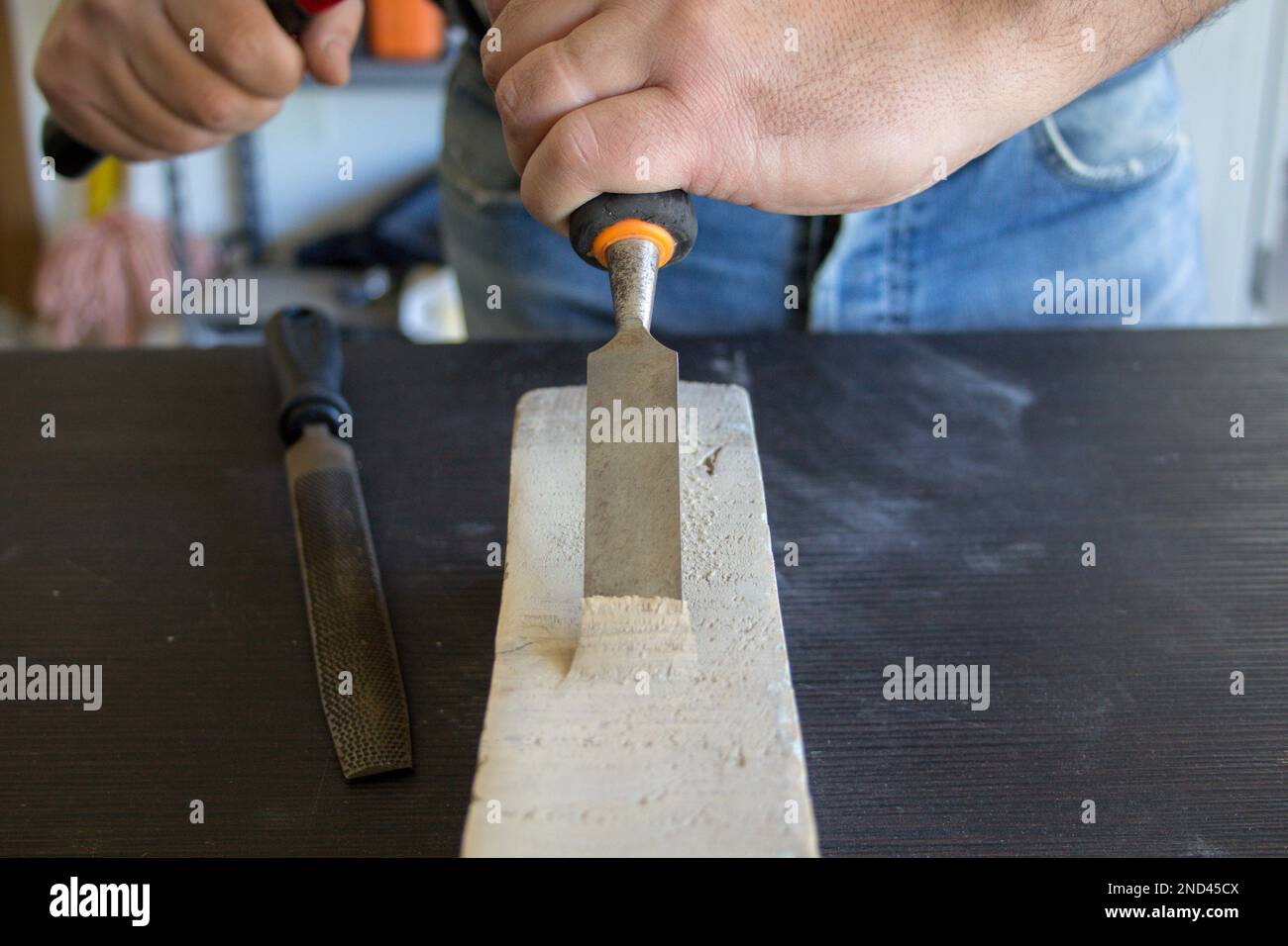 Image of a handyman craftsman's hands holding a carpenter's hammer and chisel while doing some work and carving on wood. DIY work in the laboratory. Stock Photo