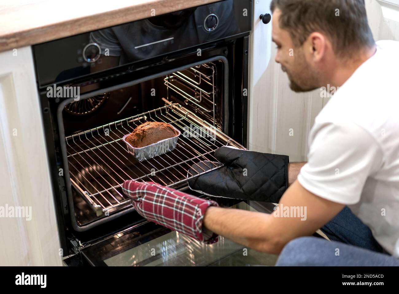 Man taking out chocolate cake from oven, man backing cake at home Stock