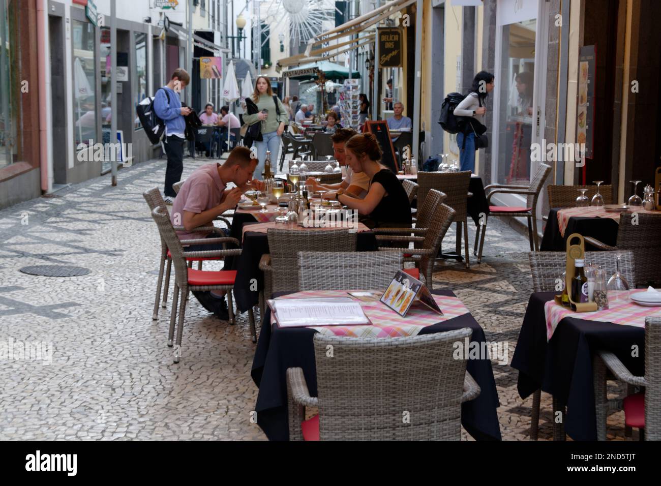 Funchal, Madeira street scene - street cafe with patrons eating. Empty tables in front. Shoppers in the background. Pedestrian only - no traffic Stock Photo