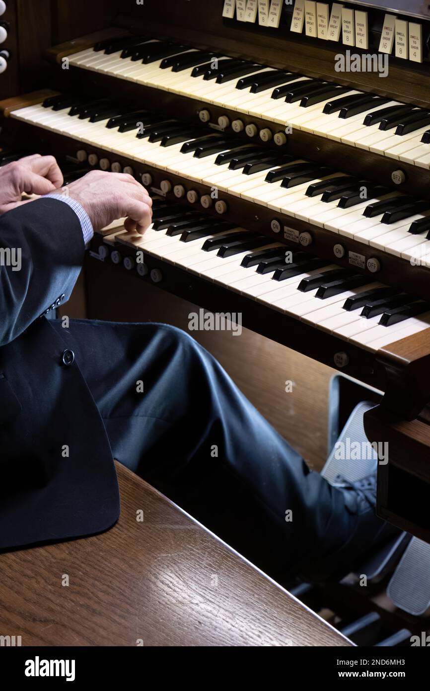 A closeup of a man playing the black and white piano-like keys of a pipe organ in church Stock Photo