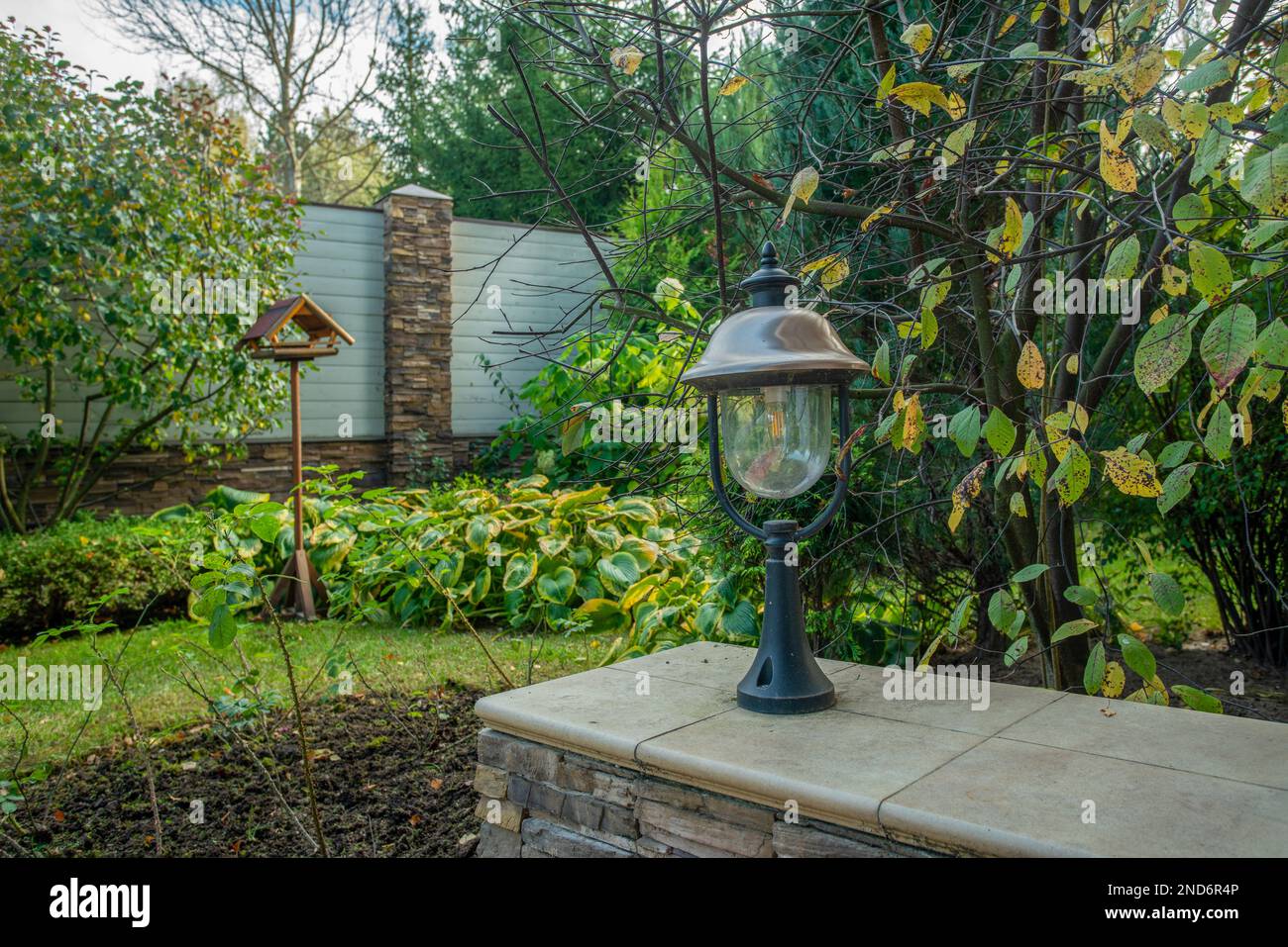 Garden in autumn and glass lantern  - Autumn Leaf color and hosts and Wooden bird feeder. Garden next to cottage in sunny autumn day Stock Photo