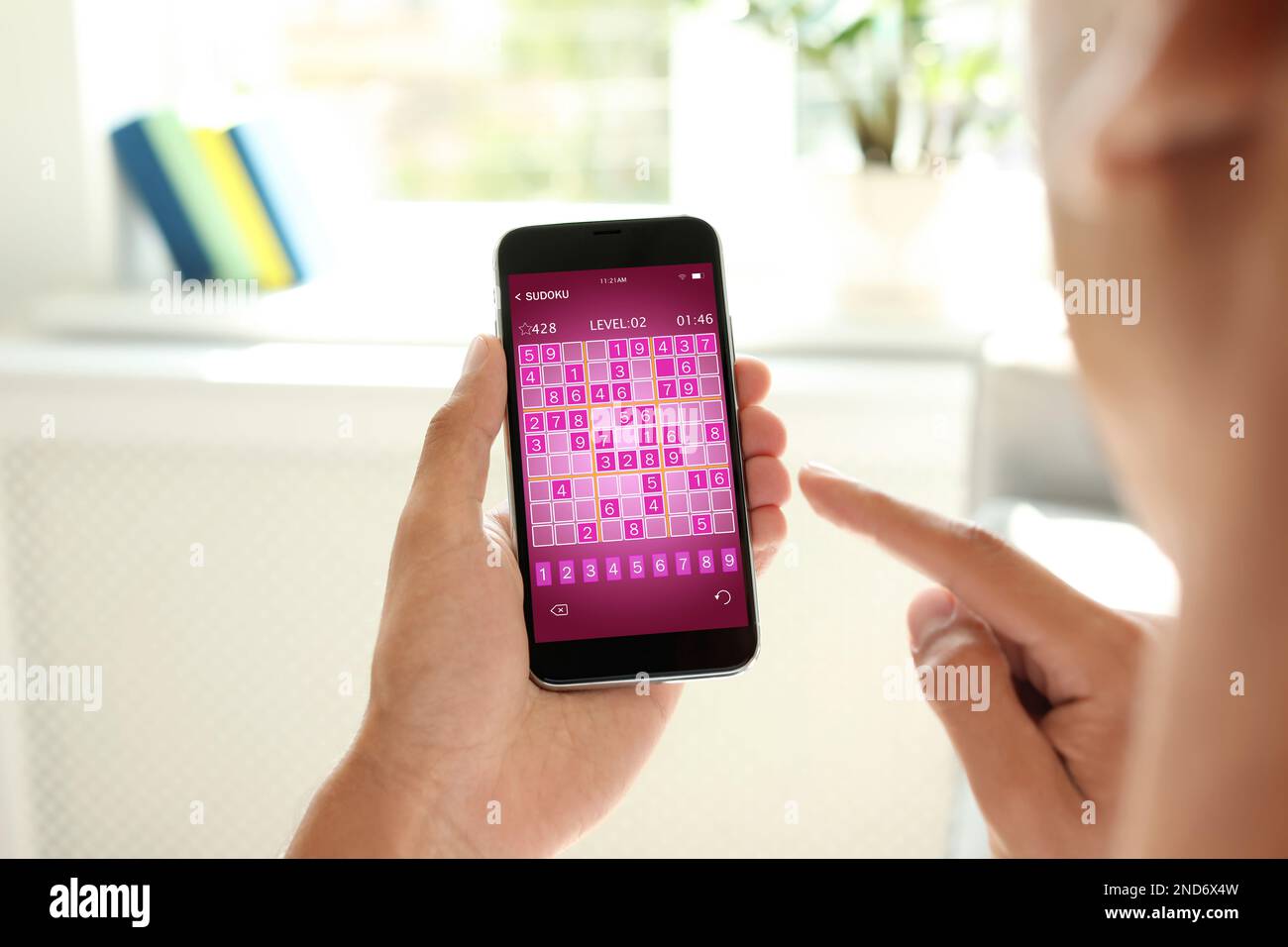 Man playing sudoku game on smartphone indoors, closeup Stock Photo
