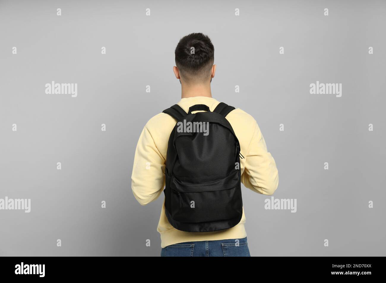Young man with stylish backpack on light grey background, back view ...