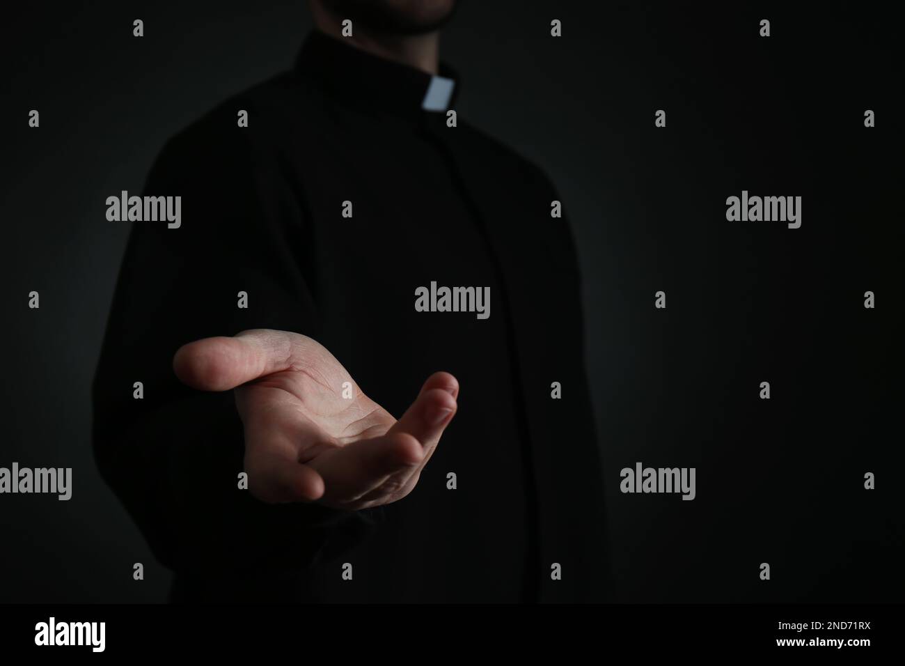 Priest reaching out his hand on dark background, closeup. Space for text Stock Photo