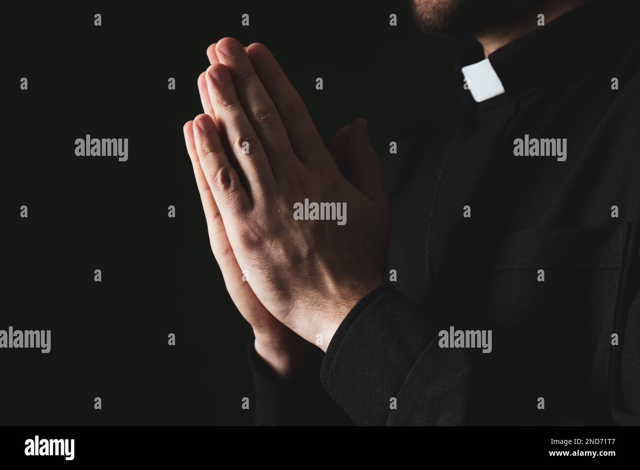 Priest in cassock praying on dark background, closeup Stock Photo