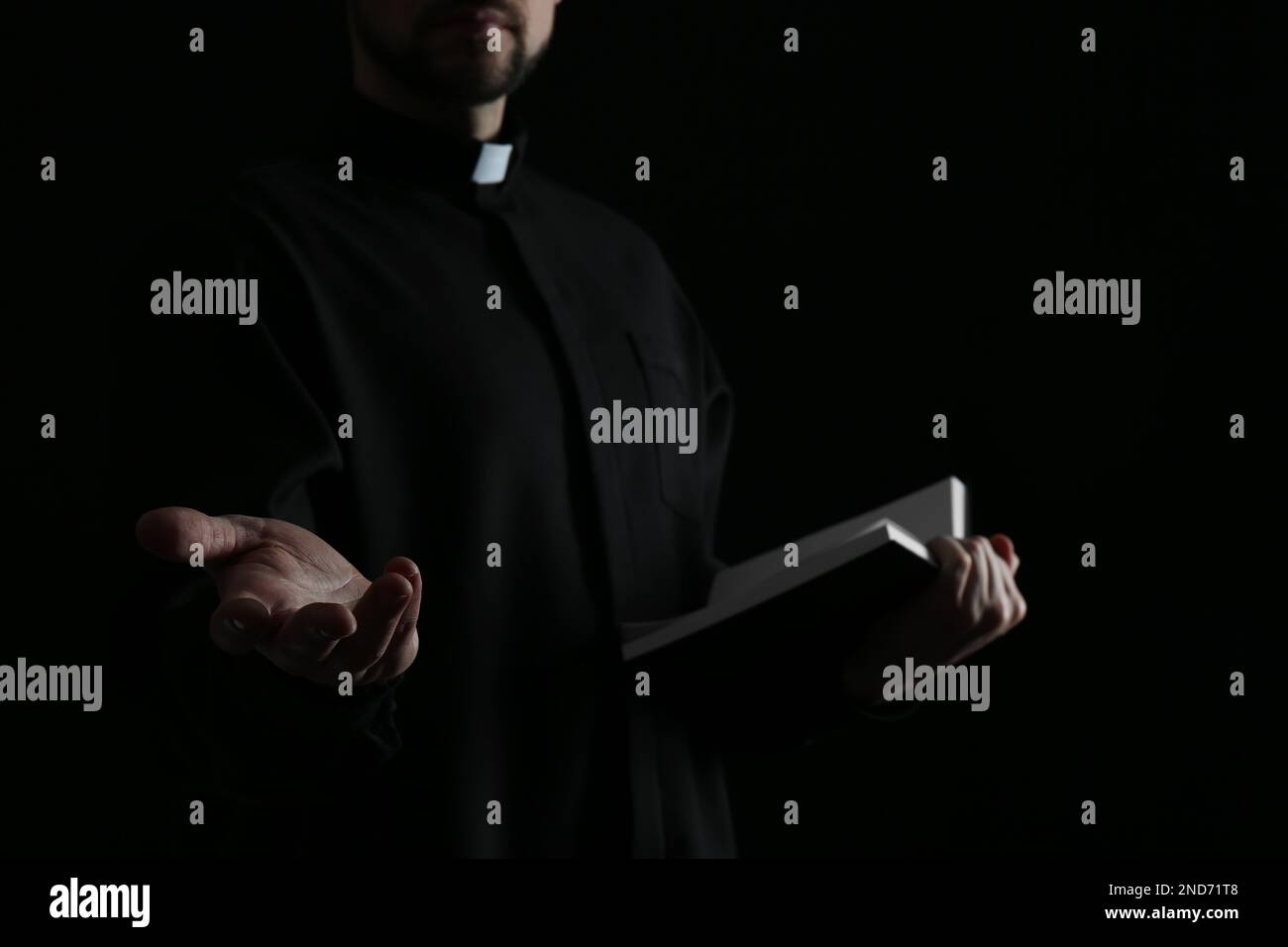Priest with Bible praying on dark background, closeup Stock Photo
