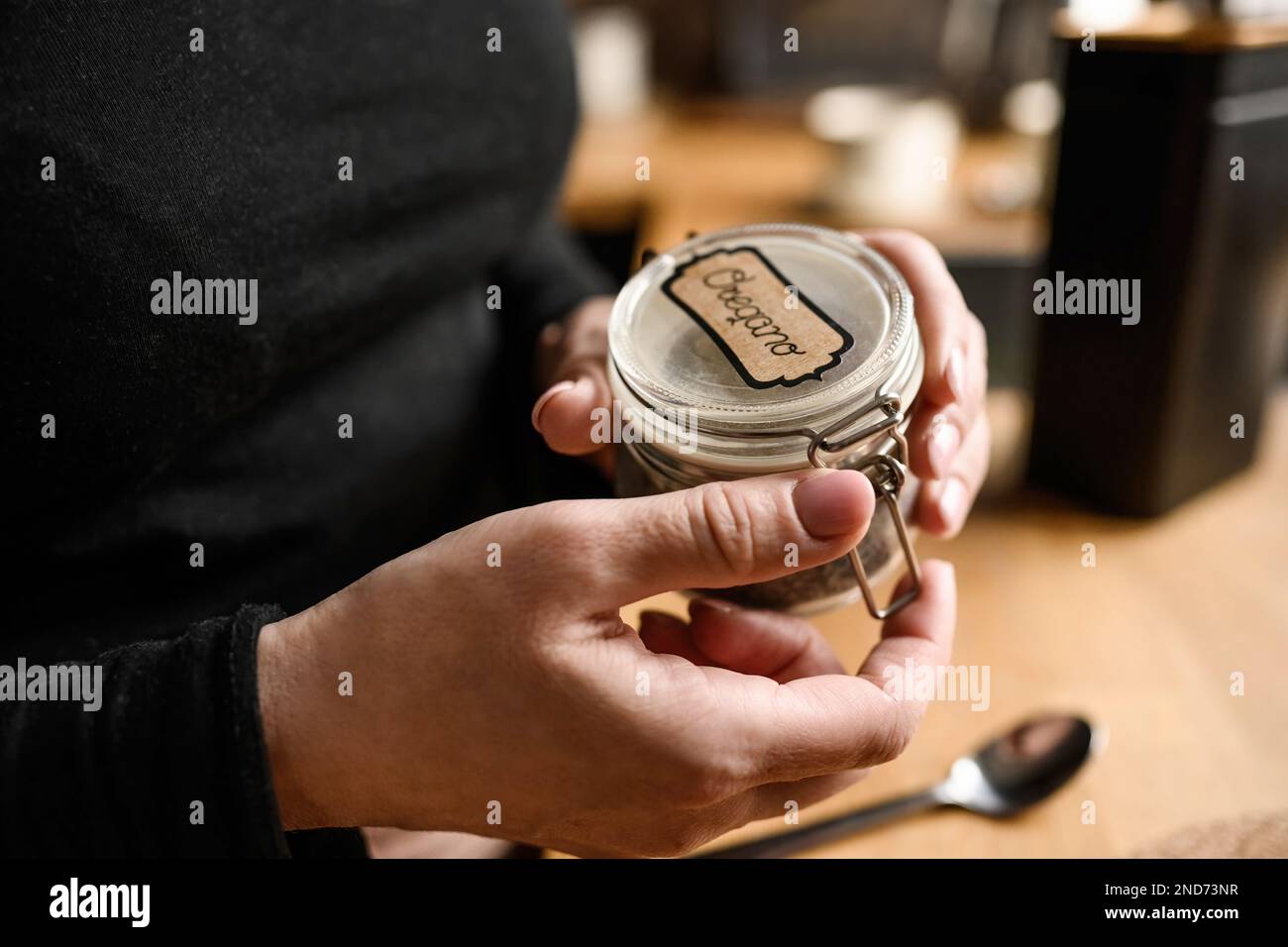 Girl hand opening jar with oregano at kitchen Stock Photo