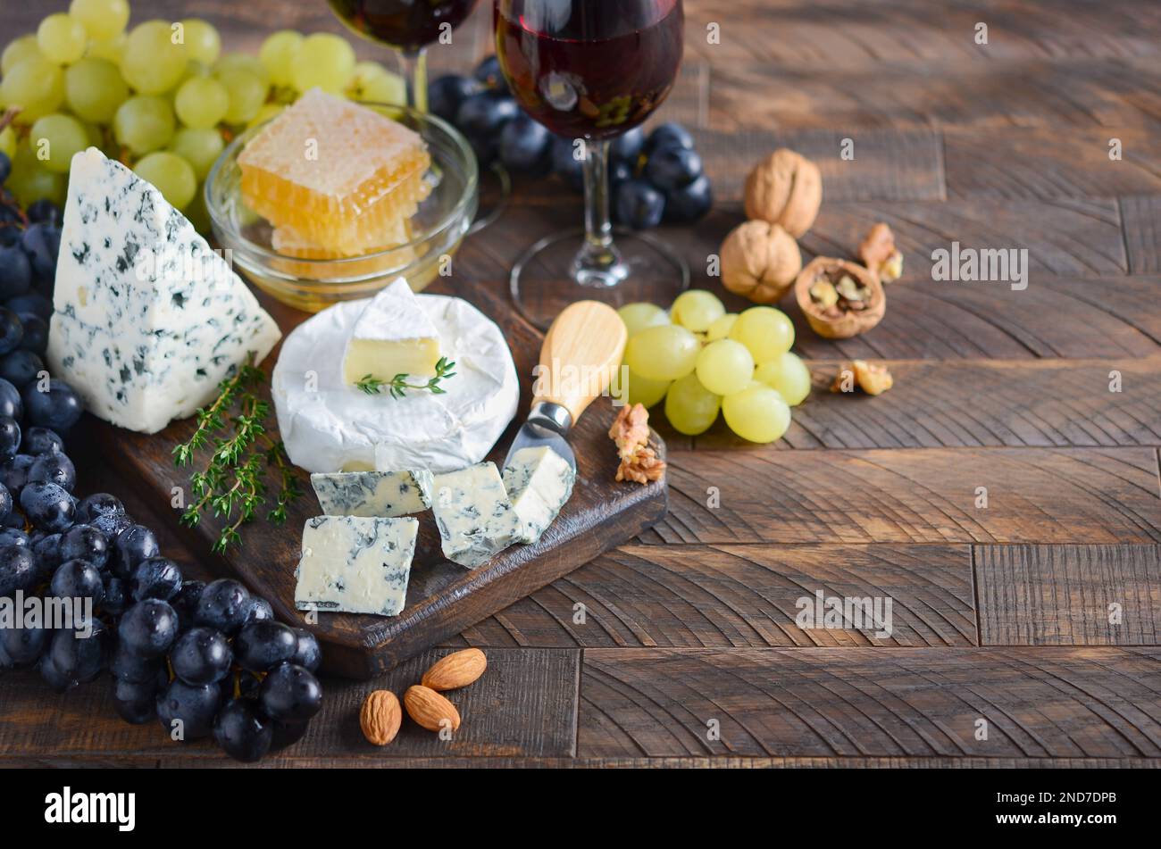 Cheese plate with grapes, honey, nuts and red wine on a wooden table. Stock Photo