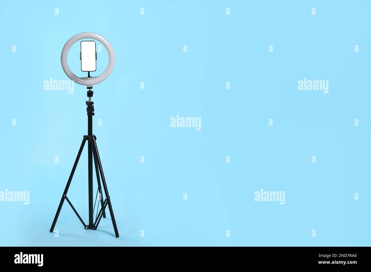 Modern tripod with ring light and smartphone on light blue background ...