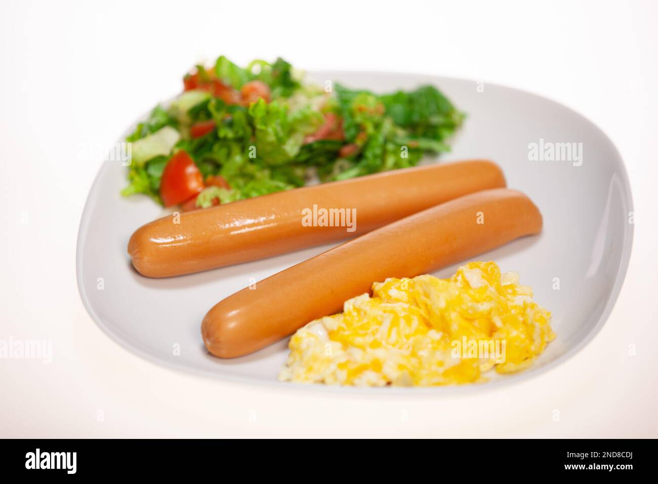 A closeup of a white plate full of sausages, yelk of an egg and salad Stock Photo