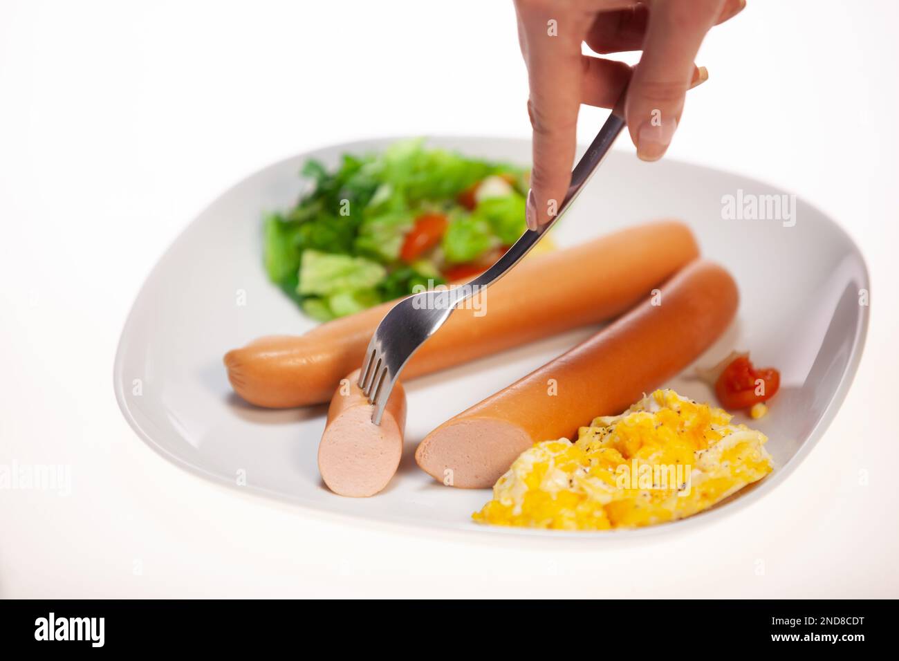 A closeup of a white plate full of sausages, yelk of an egg and salad Stock Photo