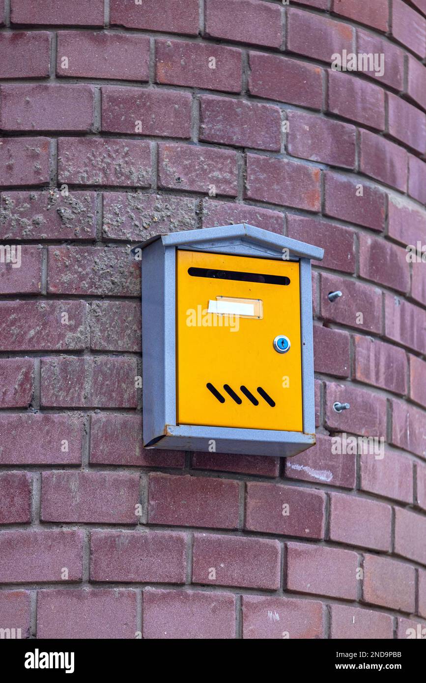 Yellow Letter Box With Lock Mounted at Purple Bricks Wall Stock Photo