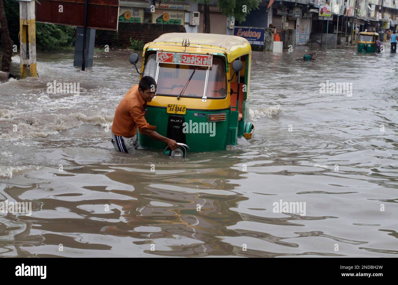 A man pulls his auto rickshaw through a flooded road after a heavy ...
