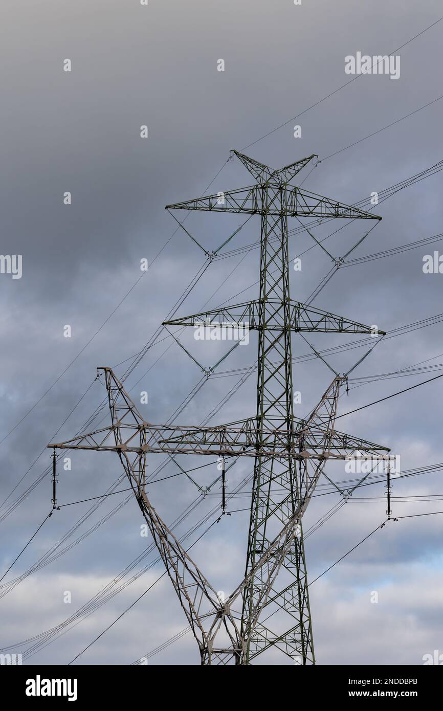 The silhouette of a high-voltage pylon against a dramatically cloudy sky. Development of high-voltage transmission networks Stock Photo