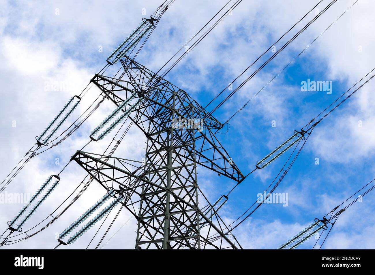 High-voltage pylon against a blue sky with a slight cloud cover. High voltage transmission lines silhouette Stock Photo