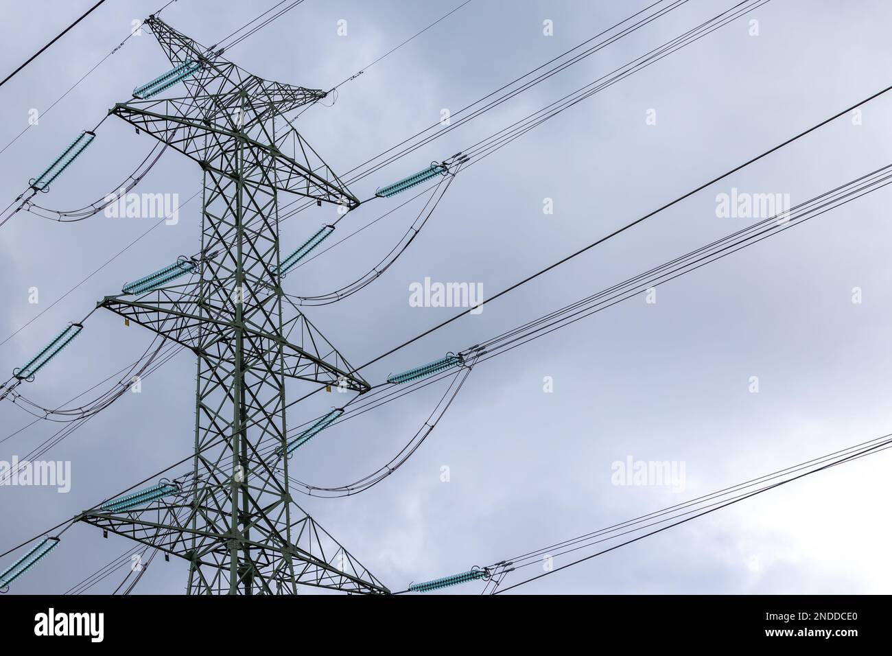 The silhouette of a high-voltage pylon against a completely cloudy sky. Development of high-voltage transmission networks Stock Photo