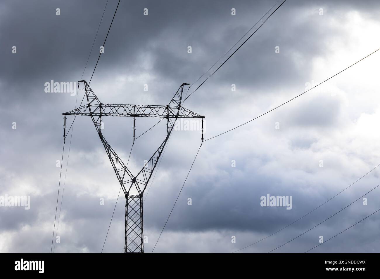 The silhouette of a high-voltage pylon against a dramatically cloudy sky. Development of high-voltage transmission networks Stock Photo
