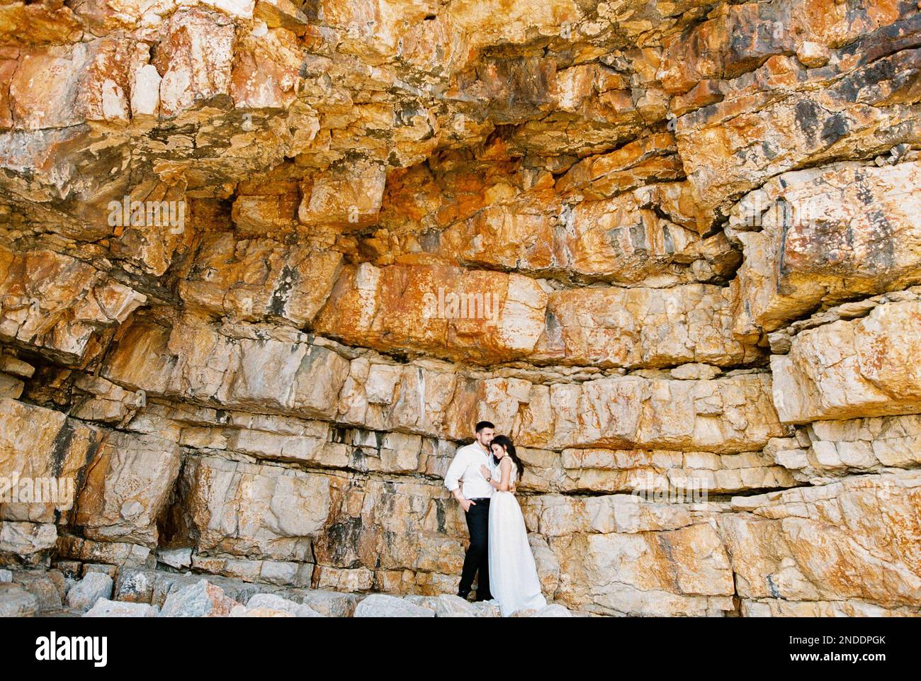 Bride and groom stand embracing near a huge rock Stock Photo - Alamy