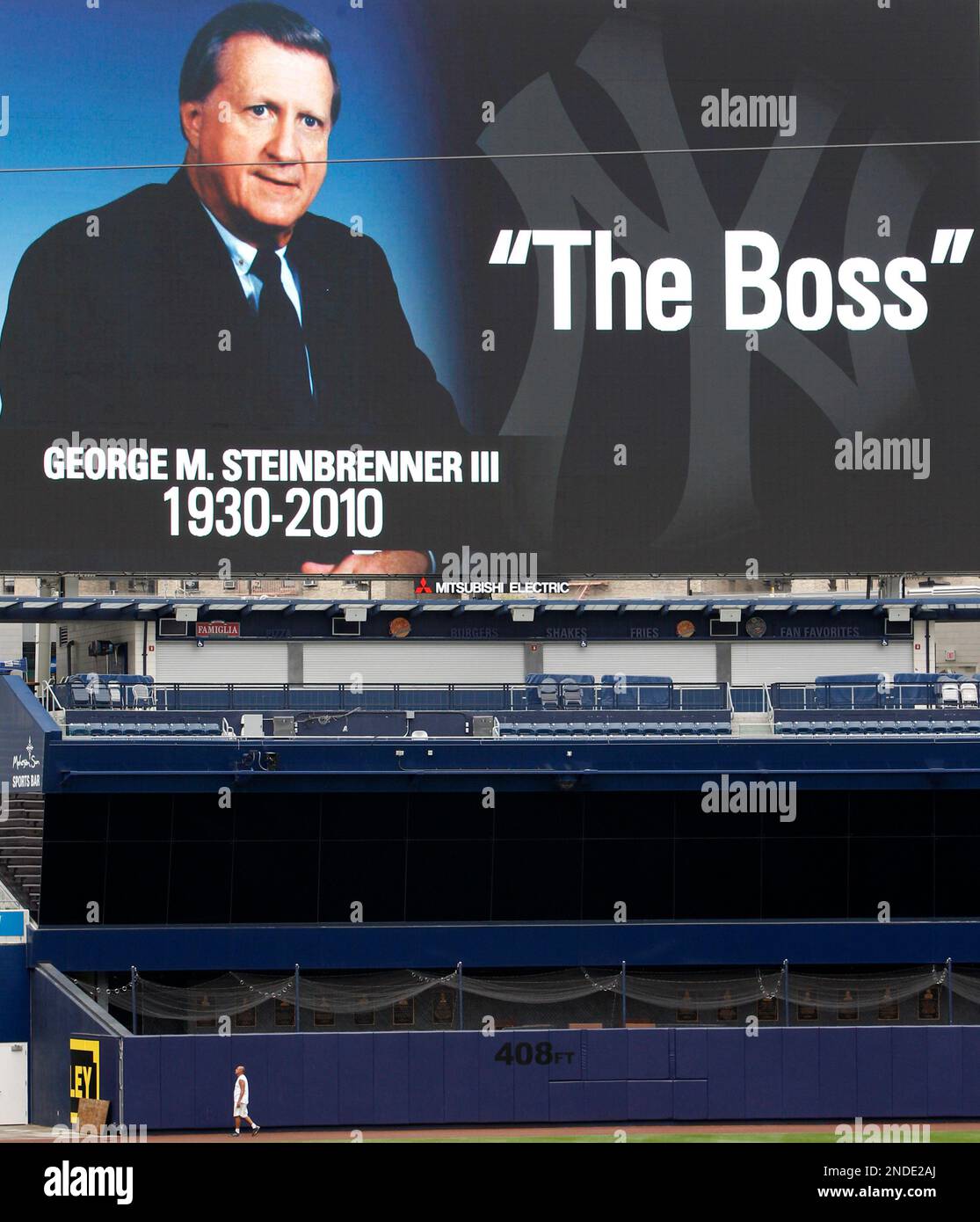 A stadium groundskeeper is dwarfed by a giant video display in memoriam