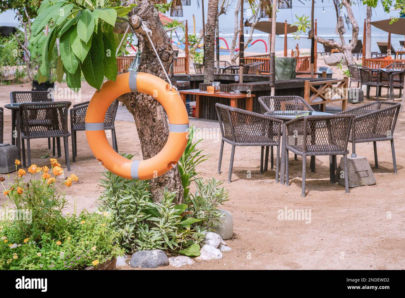 Orange rescue lifebuoy hangs on tree in front of beach restaurant at beach side, tropical Stock Photo