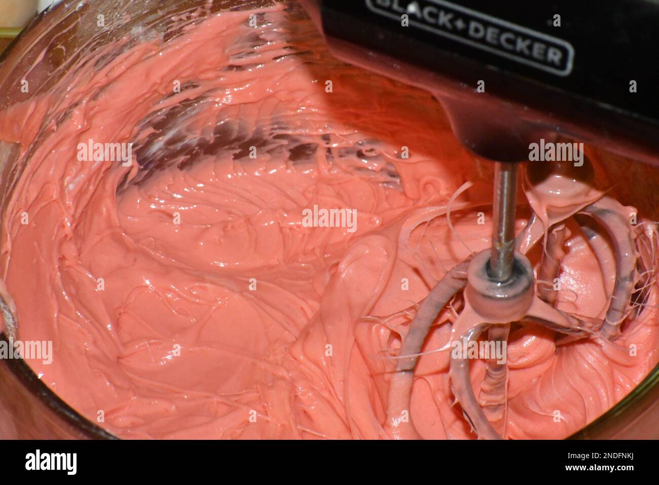 A hand mixer mixing pink cake batter in a glass mixing bowl in motion