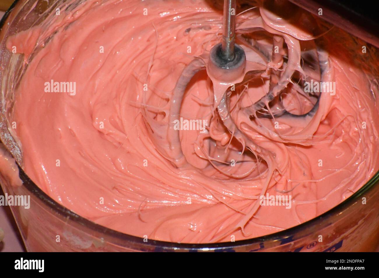A hand mixer mixing pink cake batter in a glass mixing bowl in motion