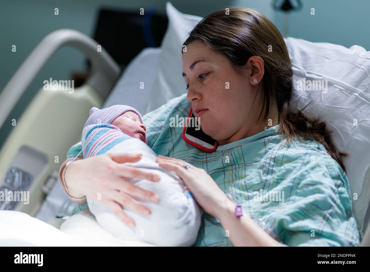 mother and her newborn baby captured in a hospital setting as the mother talks on her cell phone Stock Photo