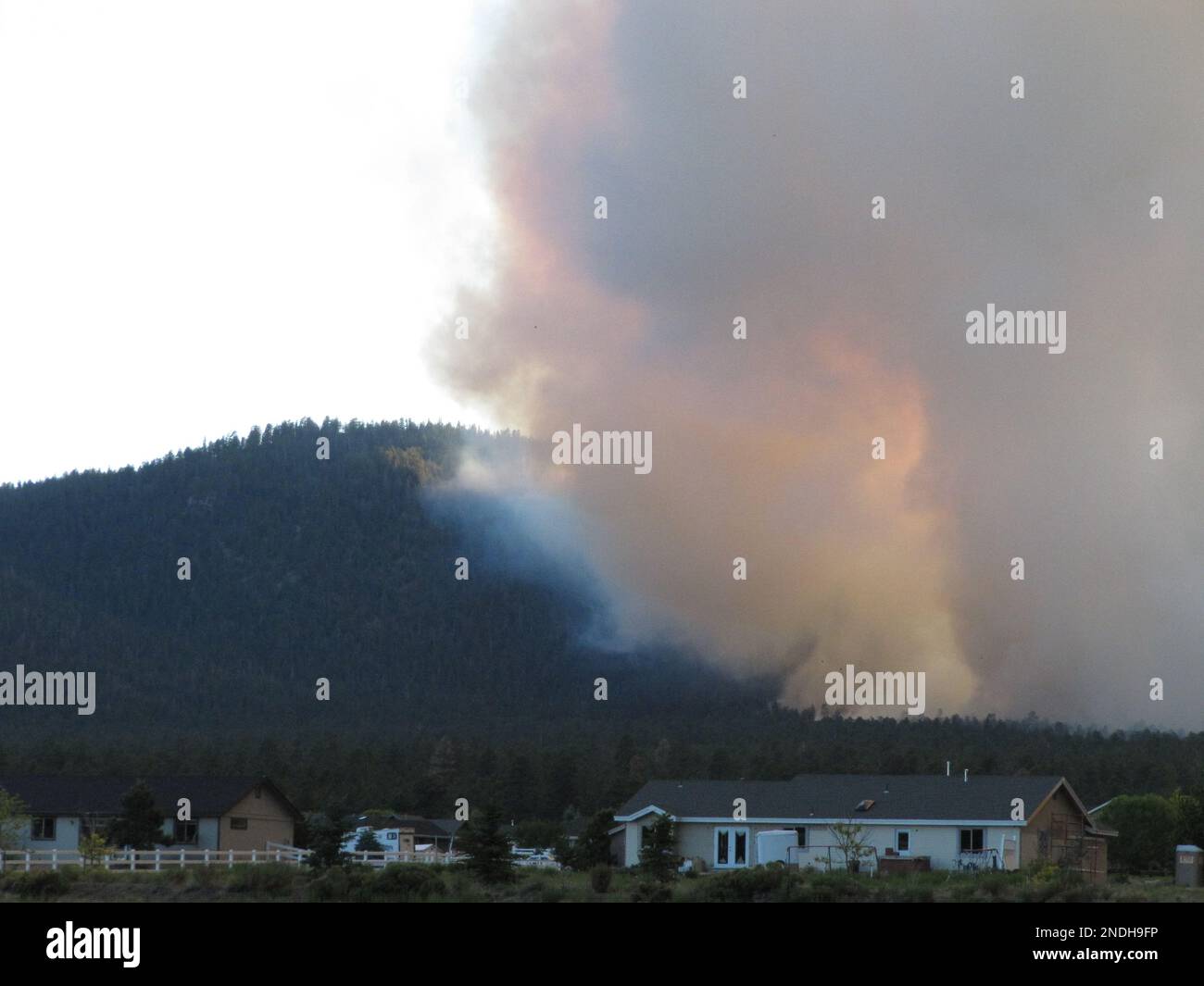 Smoke from a wildfire rises from behind homes north of Flagstaff, Ariz