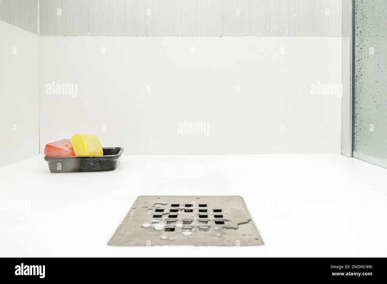 Stainless steel drain in the white resin shower tray of a glass