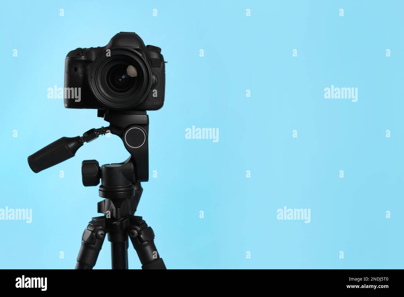 Modern tripod with professional camera on light blue background. Space ...